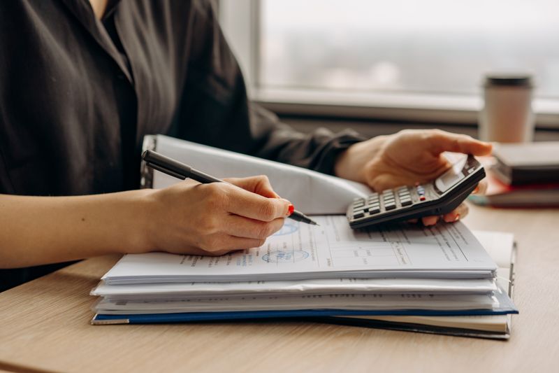 Pessoa usando calculadora e documentos financeiros sobre a mesa
